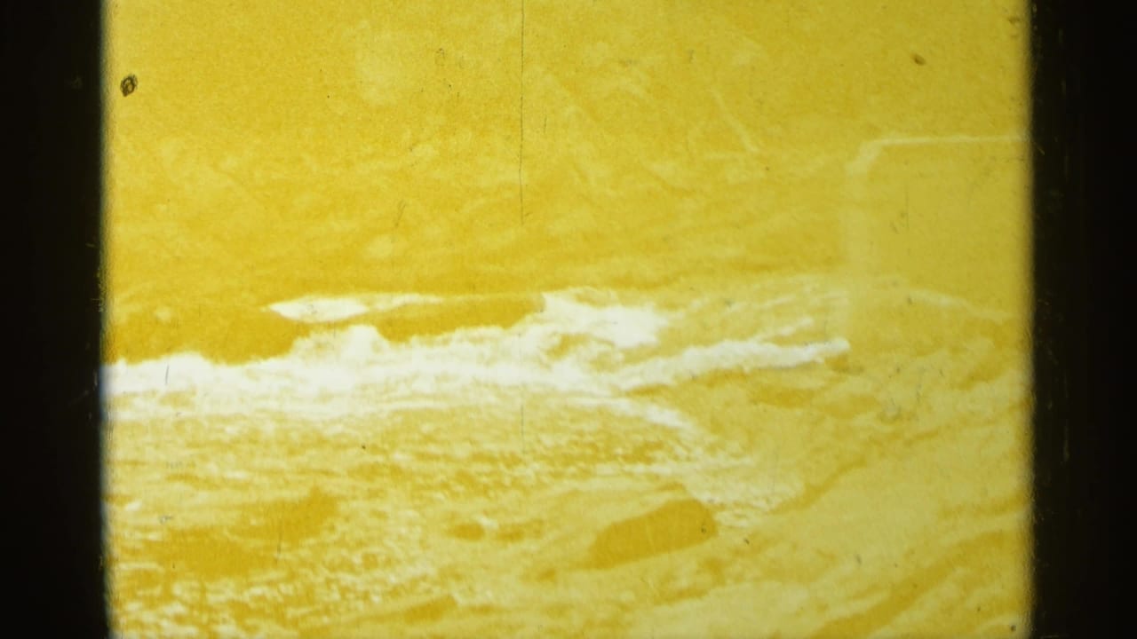 Yellow-tinted frame of rushing white water near a riverbank with dark film borders.
