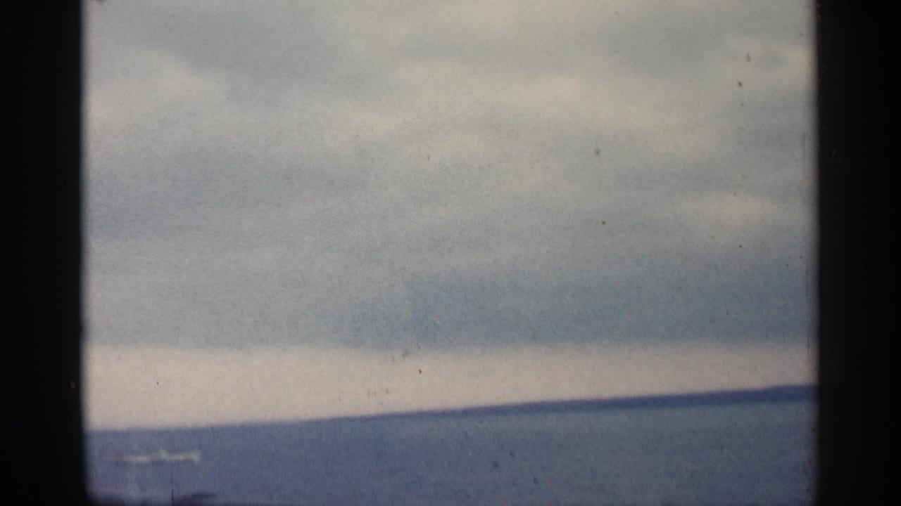 Open water and distant shore beneath a cloudy sky, with a small pale boat or wake.