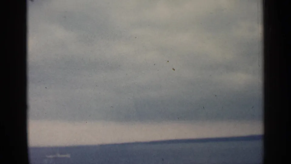 Blue-gray 8mm frame of Michigan water and distant land under an overcast sky, with visible grain and film marks.