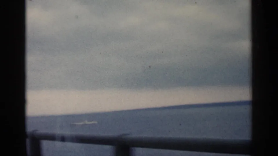1960 Michigan waterfront view through a dark divided foreground, with cloudy sky, calm water, and a low shore in the distance.