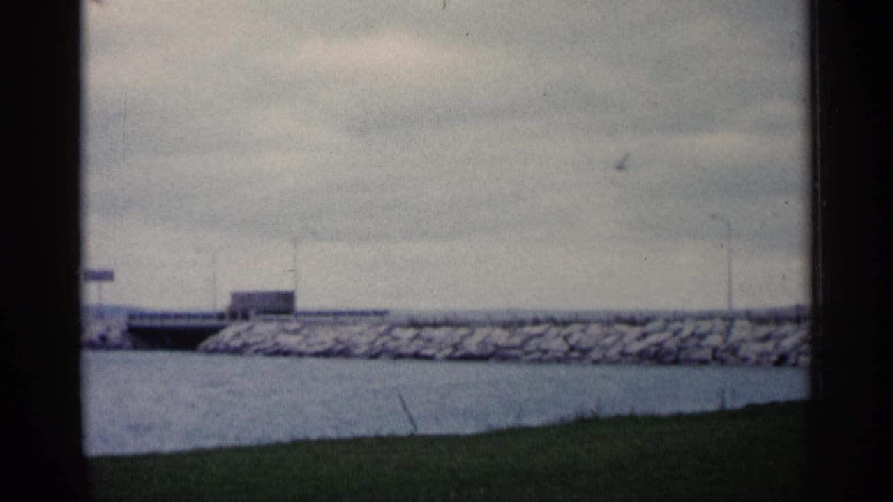 Bridge span and breakwater seen across water beneath an overcast sky.