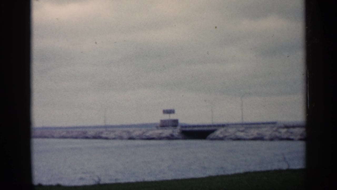 1960 Michigan 8mm frame showing open water, a long breakwater, small signs, and dark film borders.
