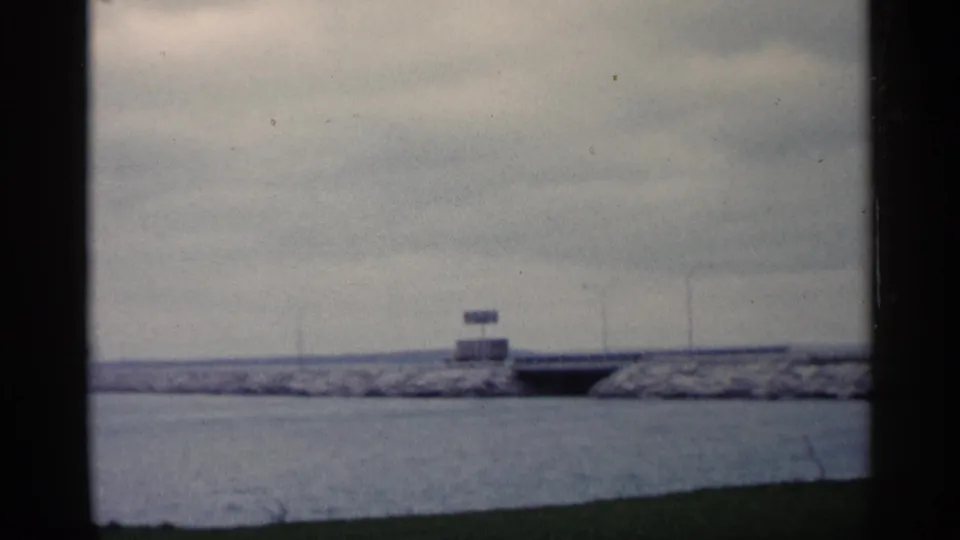 1960 Michigan 8mm frame showing open water, a long breakwater, small signs, and dark film borders.