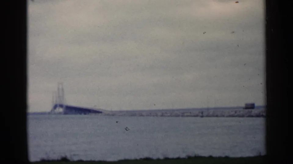 Long bridge structure over water in Michigan, filmed at a distance on 8mm with faded color and visible frame edges.