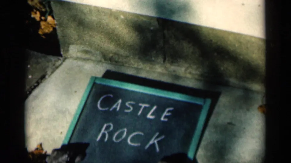 Close 8mm frame of the Castle Rock chalkboard sign on pavement, with darker exposure, leaves, and sidewalk lines visible.