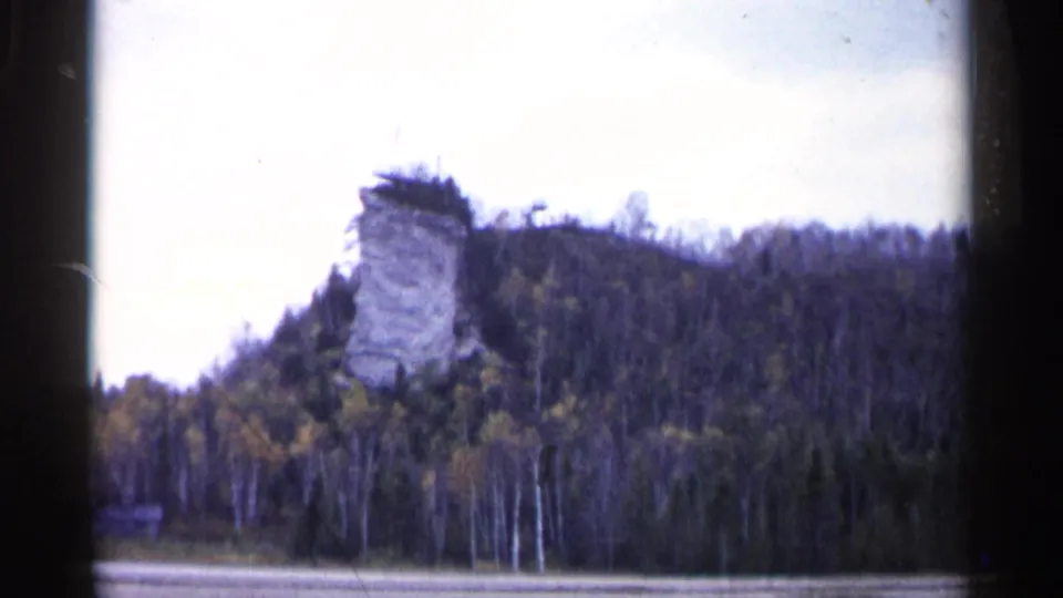 Distant 1960 Michigan view of Castle Rock rising from a forested hillside beyond a pale waterline.