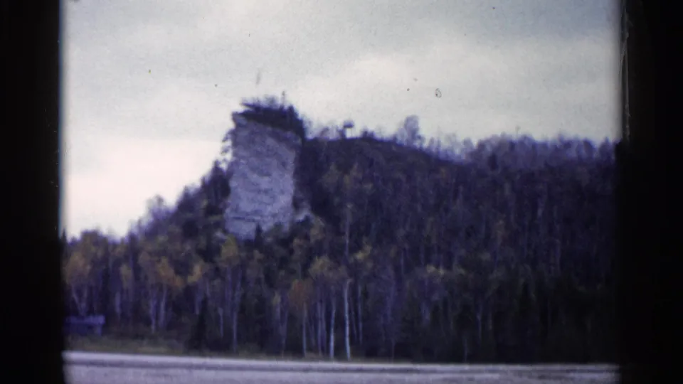 1960 Michigan 8mm frame showing a pale limestone cliff above dense trees and a muted sky.