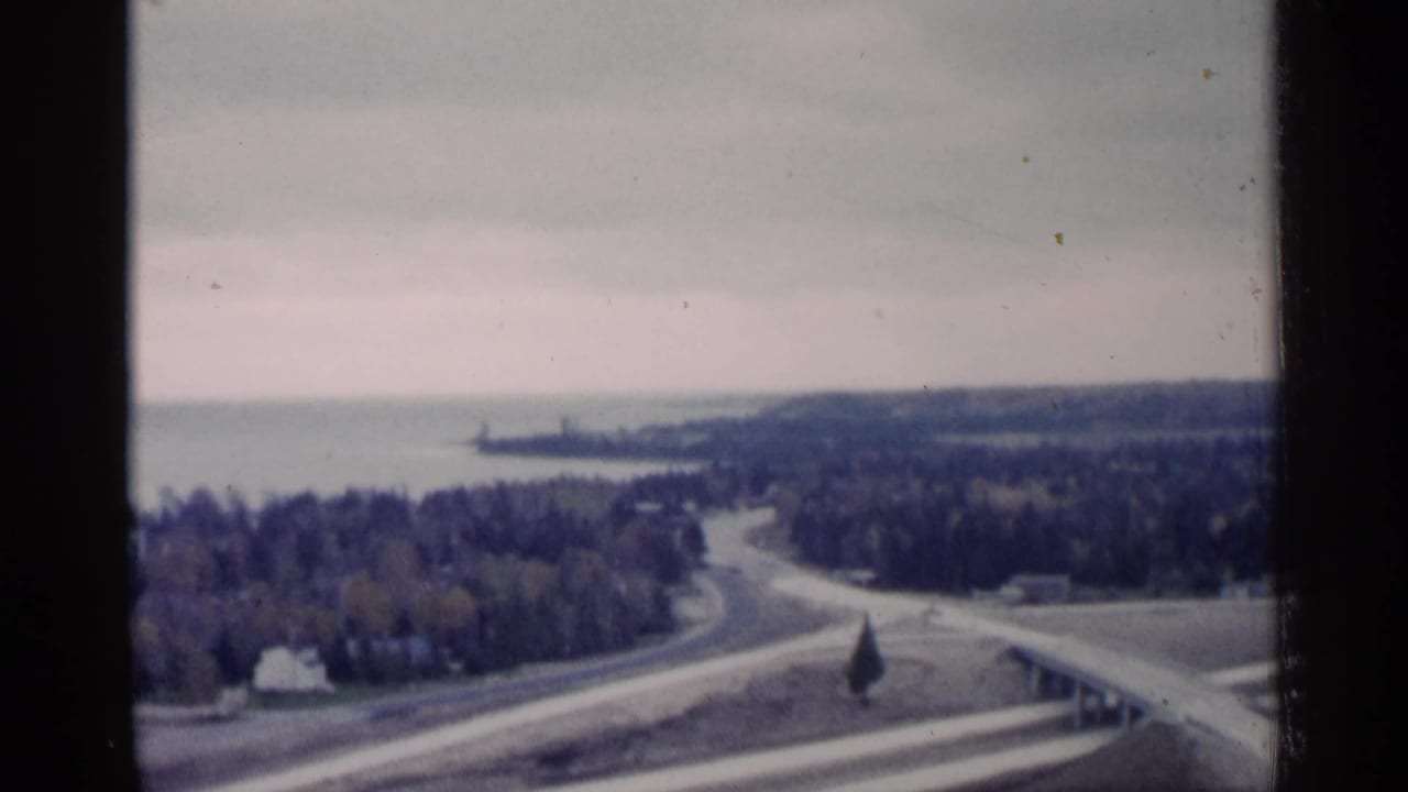 Elevated view of a winding road leading through woods toward a lake.