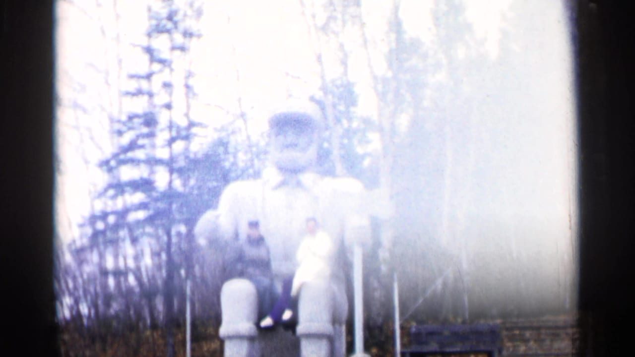 Large bearded statue partly overexposed with two adults seated near its front.
