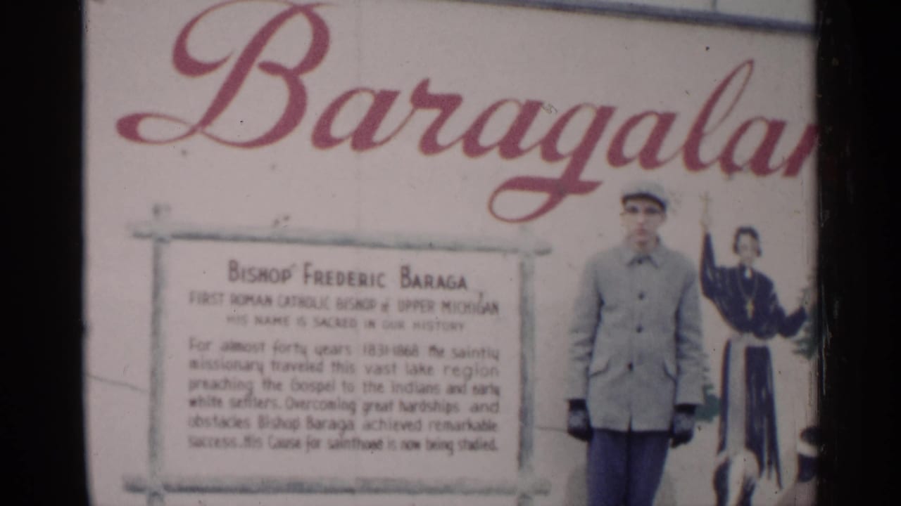 1960 Michigan 8mm frame showing a Bishop Frederic Baraga display sign with a man standing near the right edge.
