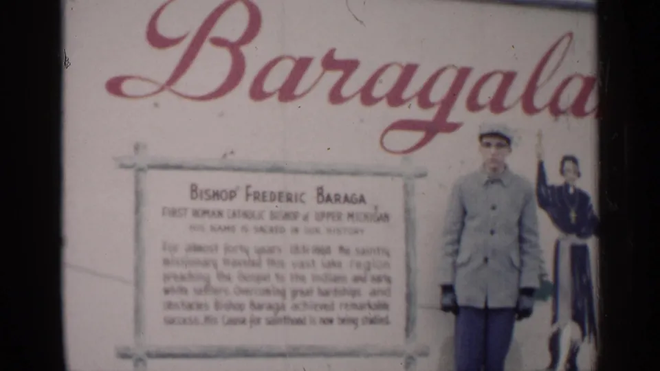 Similar 1960 Michigan frame of the Bishop Baraga marker display, with an adult man standing beside the text panel.