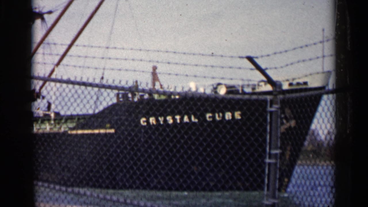 The tanker Crystal Cube remains docked behind fencing, with deck fittings and barbed wire visible above the hull.
