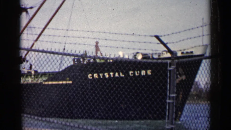 The tanker Crystal Cube remains docked behind fencing, with deck fittings and barbed wire visible above the hull.