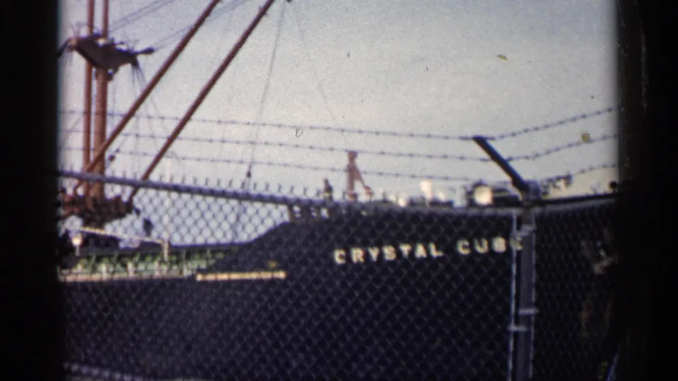 A shifted 1960 Michigan view shows the Crystal Cube hull partly cropped behind the fence, with mast and rigging above the deck.