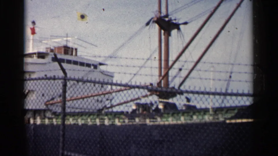 1960 Michigan 8mm frame with the ship superstructure more centered, a small flag above it, and fence wire cutting across the dockside view.