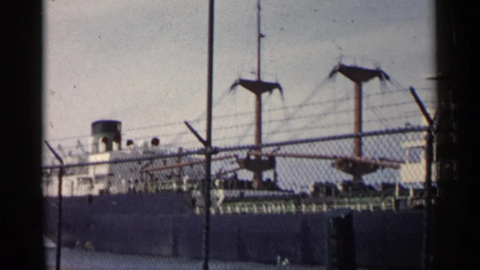 A final 1960 Michigan frame shows the ship lower in view, with masts, fence mesh, and dockside barriers dominating the foreground.
