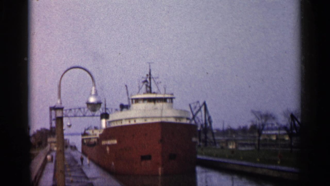 Red freighter sits in a canal lock beside a wet walkway and curved lamppost.