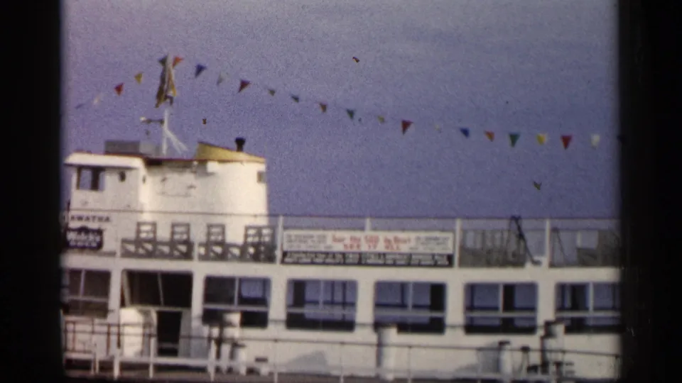 1960 Michigan 8mm frame showing the left portion of a white docked passenger boat with deckhouse, railings, and bunting.