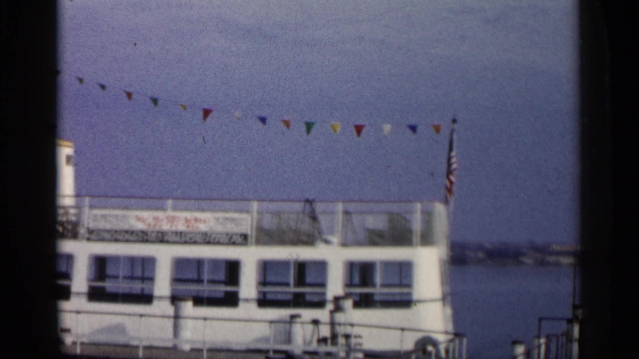 White tour boat docked on a river with pennant flags overhead.