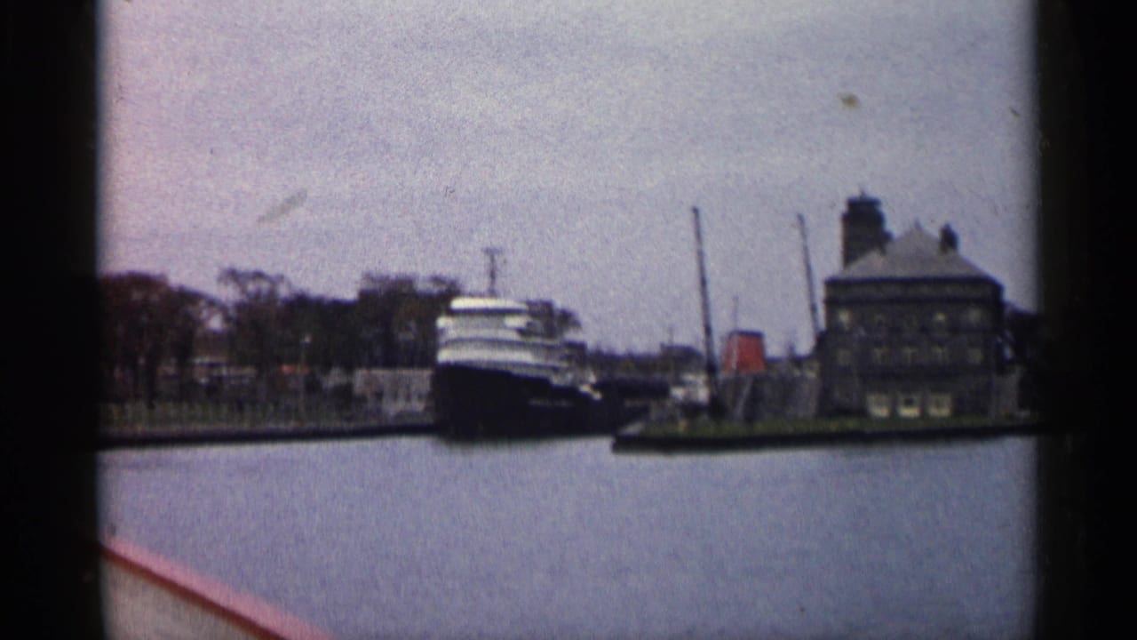 1960 Michigan home-movie frame showing a large freighter near an industrial waterfront building under an overcast sky.