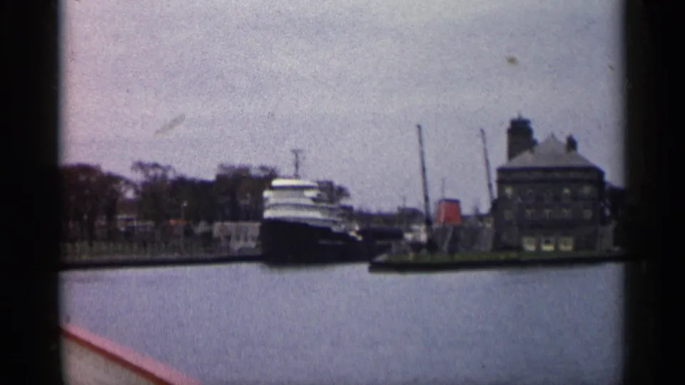 1960 Michigan home-movie frame showing a large freighter near an industrial waterfront building under an overcast sky.