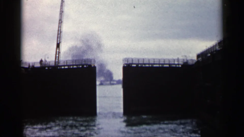 1960 Michigan home-movie view through open lock gates toward water, haze, and distant harbor structures.
