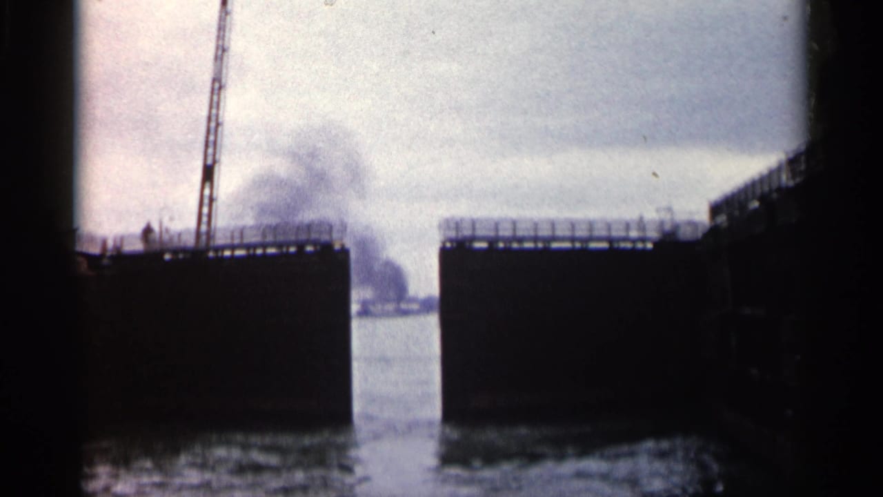 1960 Michigan 8mm frame showing dark lock walls, open gates, a crane on the left structure, and rippling water in the channel.