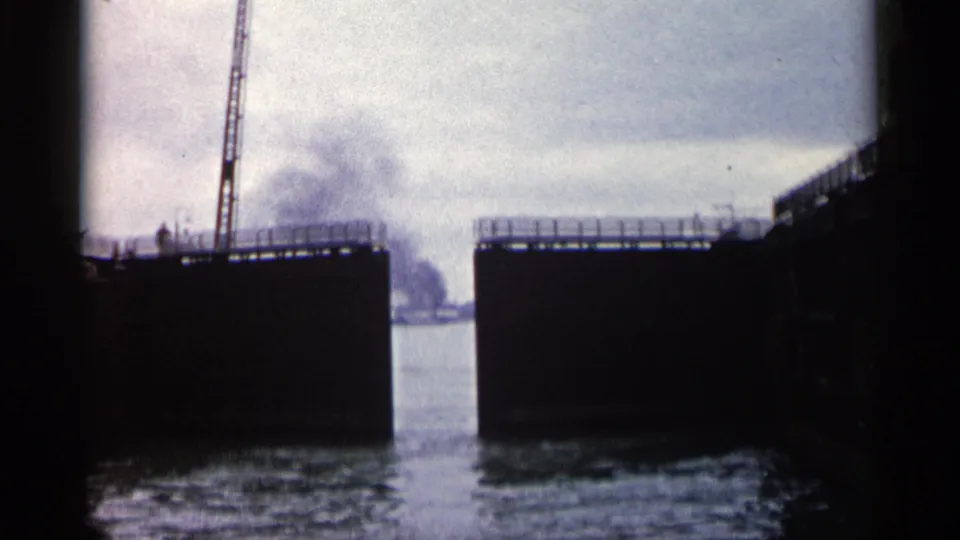 Boat-facing view through a Michigan lock system, with massive dark gate sections, calm water, and faint smoke or haze beyond.