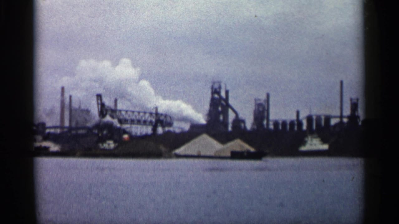 Industrial complex across water with smoke rising from chimneys.