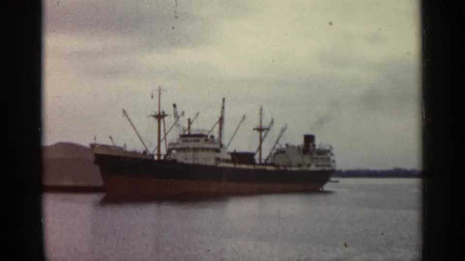 The cargo vessel fills the frame in a 1960 Michigan harbor view, with deck equipment silhouetted against cloudy sky.