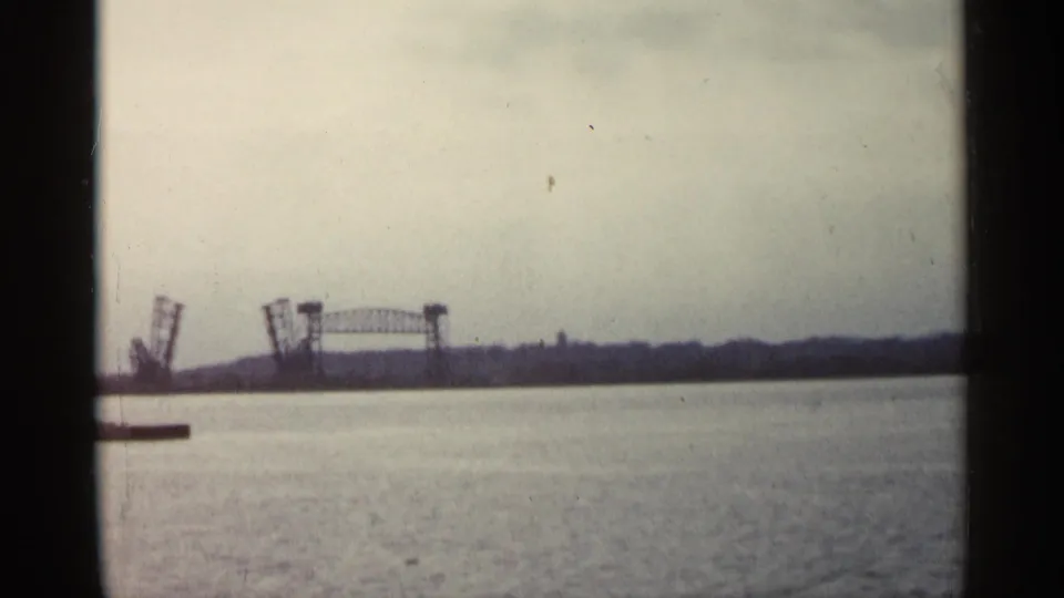 1960 Michigan 8mm frame showing a raised drawbridge in the distance across calm water beneath an overcast sky.