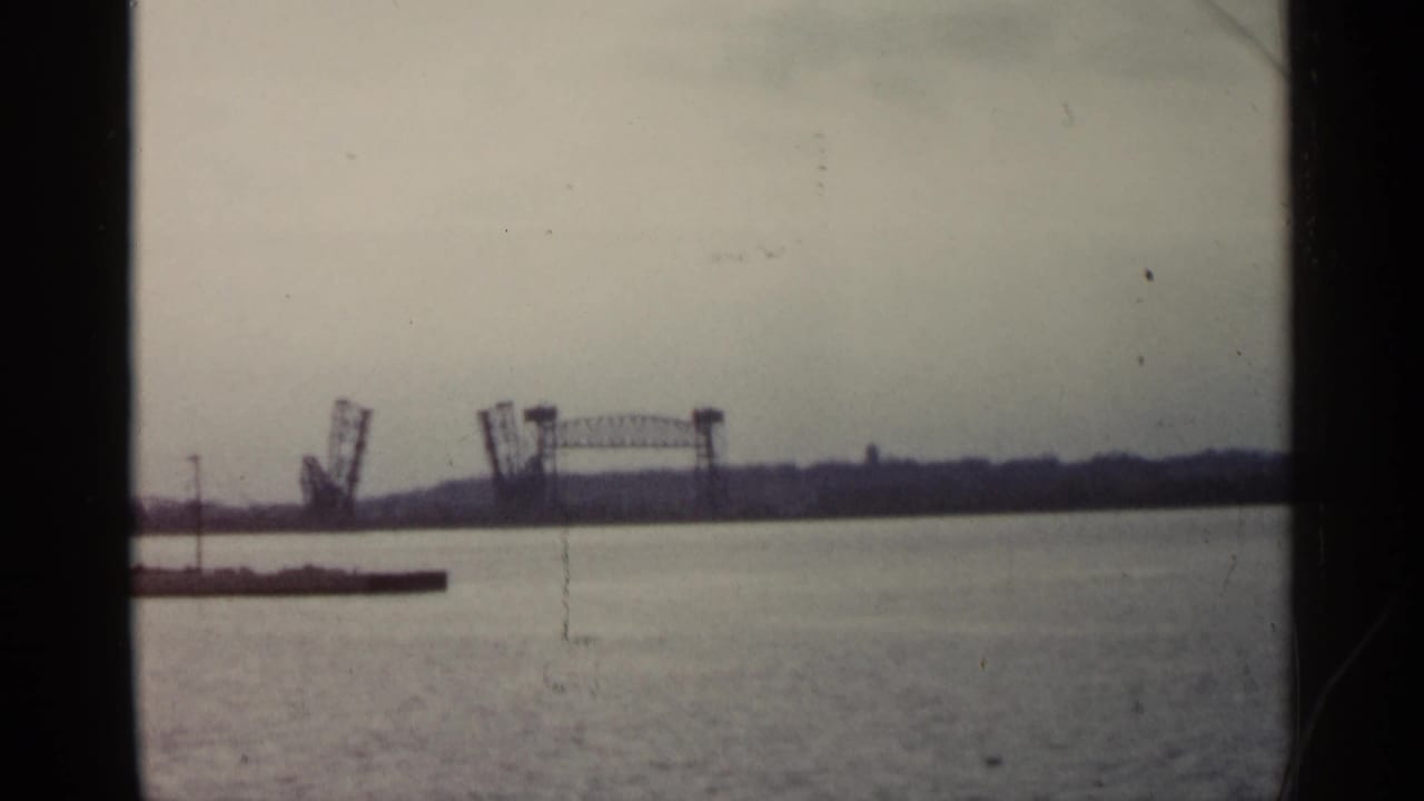 Raised drawbridge and distant shoreline viewed over water.