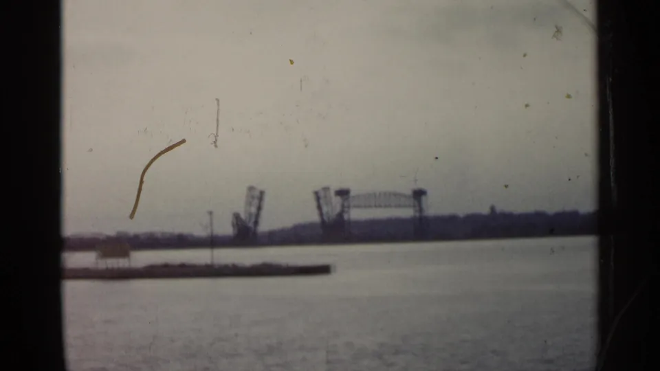 1960 Michigan waterfront view with a low pier or breakwater in the foreground and a raised drawbridge in the distance.
