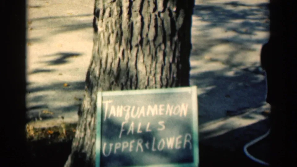 1960 Michigan home-movie frame showing a tree and a hand-painted sign reading Tanguamenon Falls Upper and Lower.