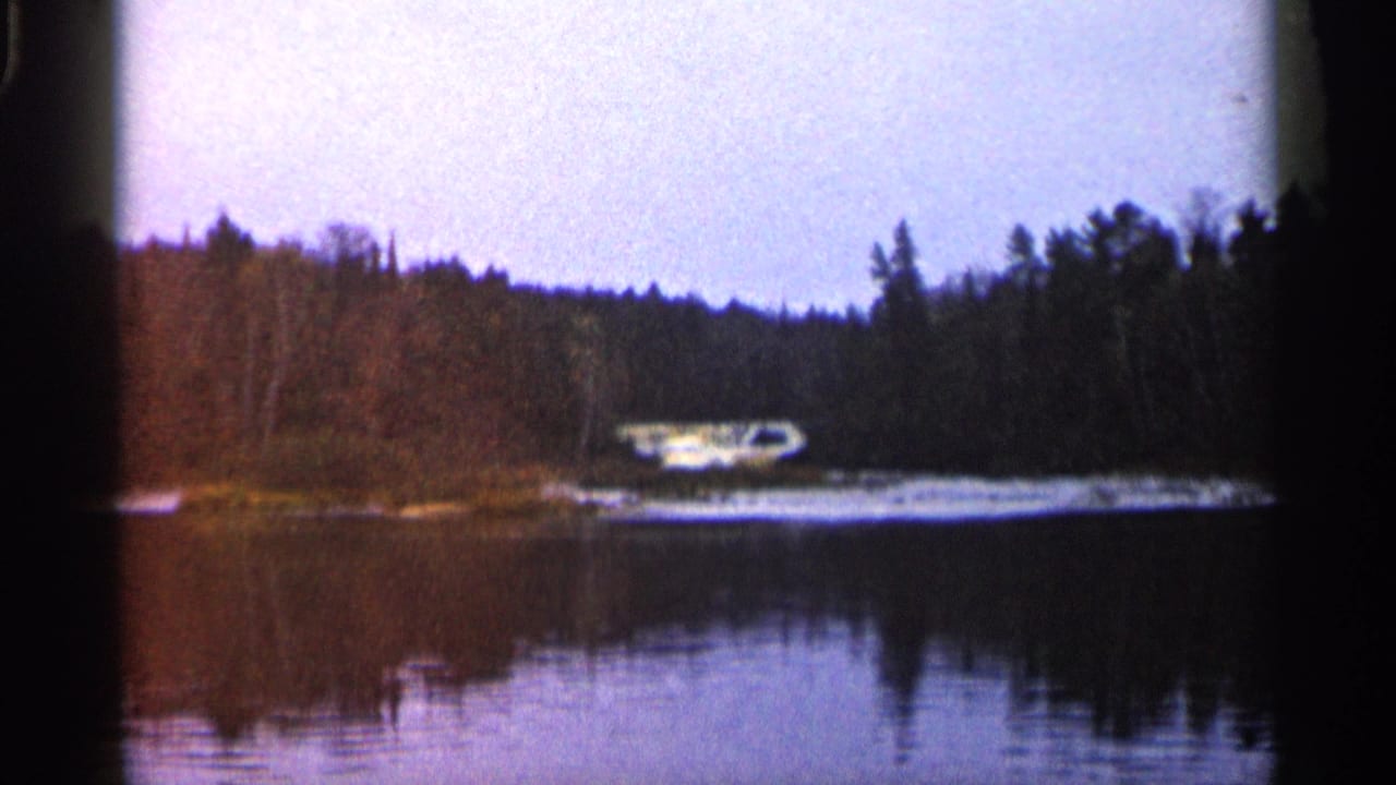 Wooded lake shoreline with a small white boat and reflections in the water.