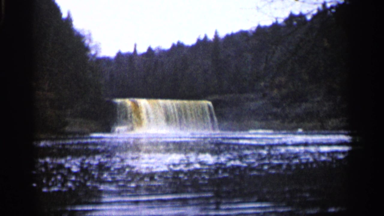 Waterfall spills over a broad ledge with ripples spreading across the foreground pool.