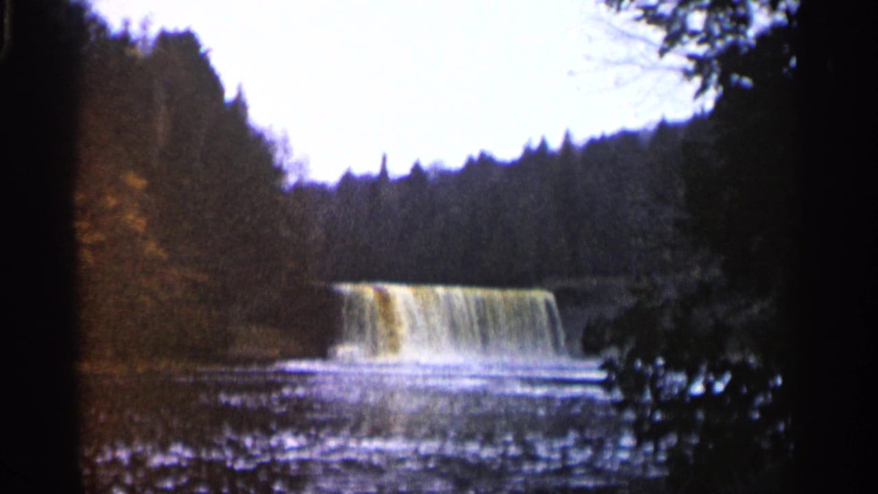 Waterfall spilling across a low ledge in a wooded stream.