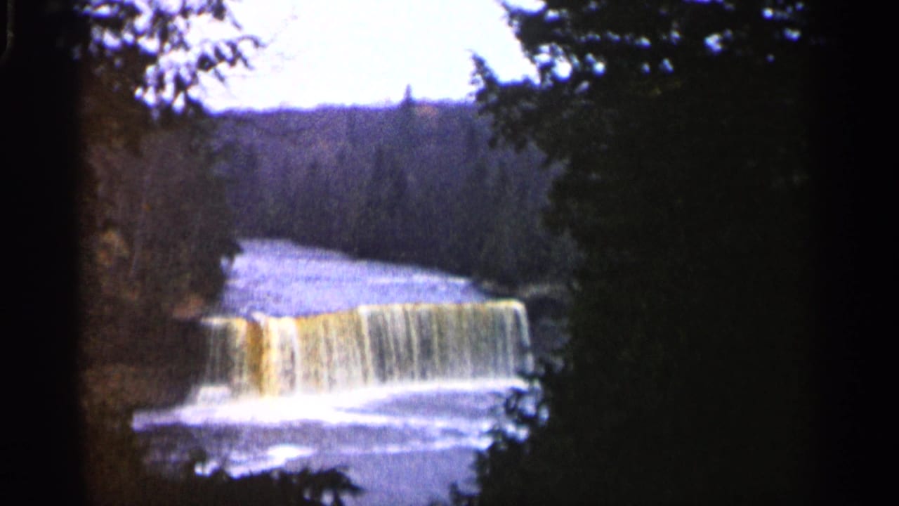 1960 Michigan 8mm frame showing a small waterfall over a ledge, with dark trees around the waterway.