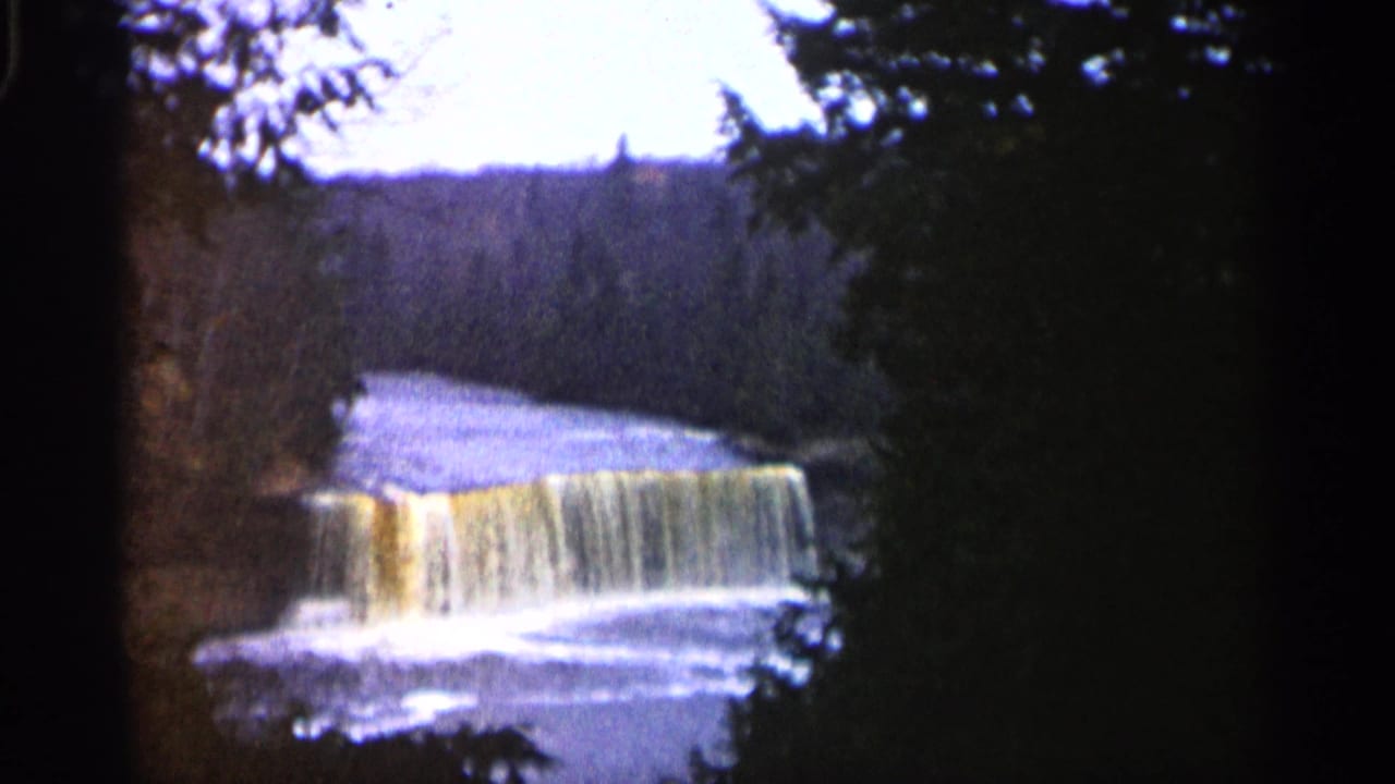 Small waterfall and river seen through dark tree framing.