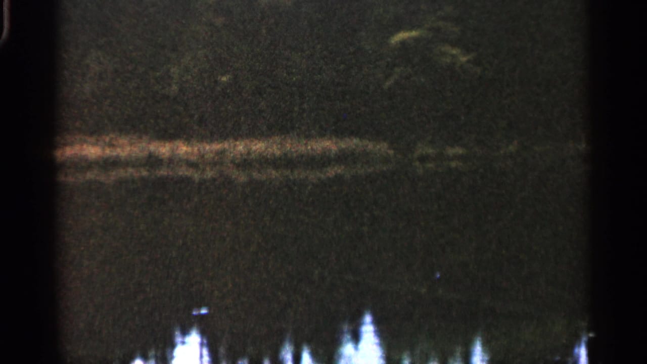 1960 Michigan 8mm frame with a soft horizontal reflection across dark water and indistinct bright forms below.