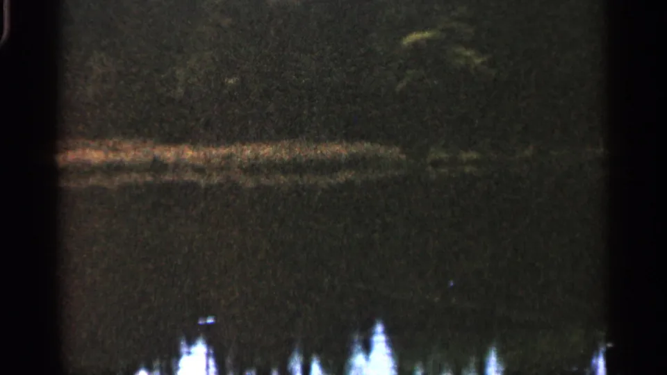 1960 Michigan 8mm frame with a soft horizontal reflection across dark water and indistinct bright forms below.