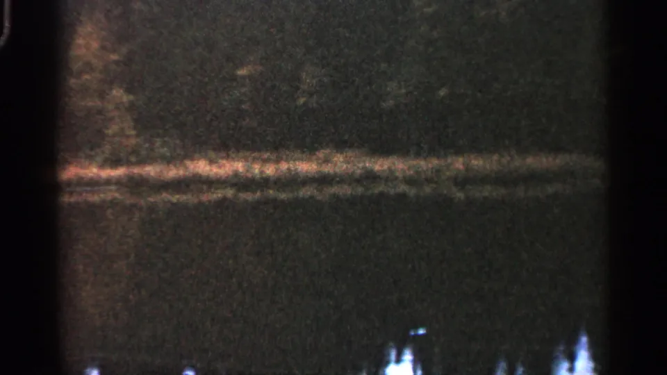 1960 Michigan 8mm frame with a dark water surface, muted shoreline reflection, and bright lower-edge highlights.
