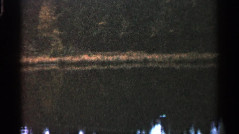 1960 Michigan 8mm frame showing a dim wooded shoreline reflected in still lake water, with grain and dark gate edges.