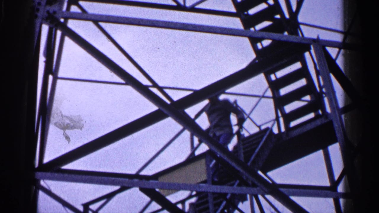 Man climbing metal stairs inside a steel tower, seen through diagonal braces against pale sky.