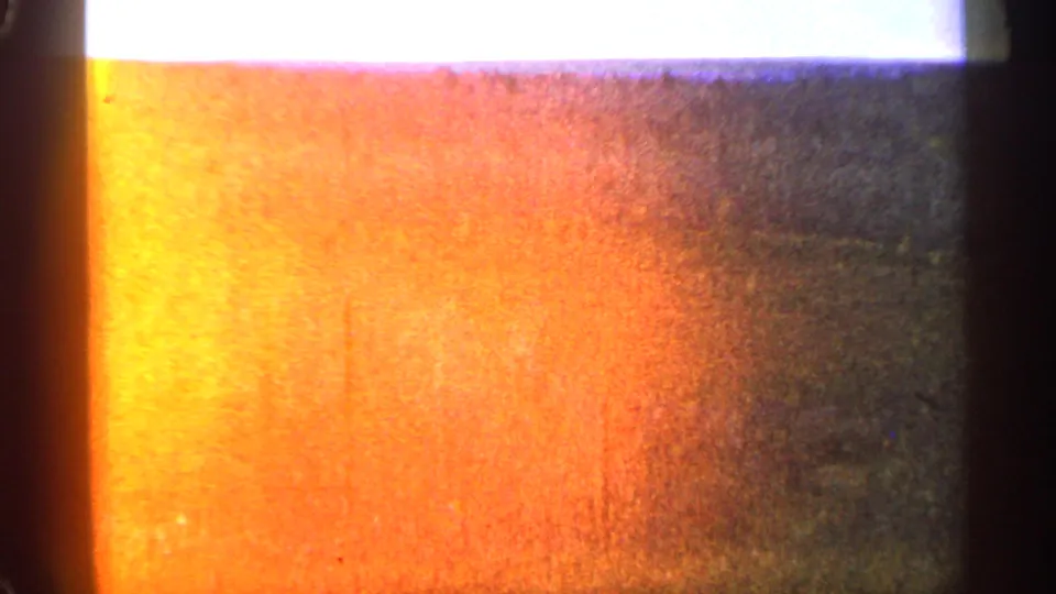 1960 8mm frame with strong orange light leak or exposure flare over the meadow scene.