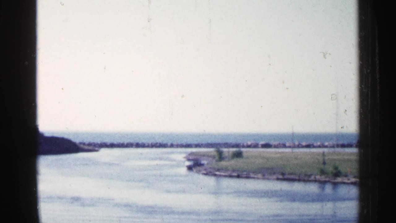 Calm waterway and grassy shoreline seen through a dark window frame.
