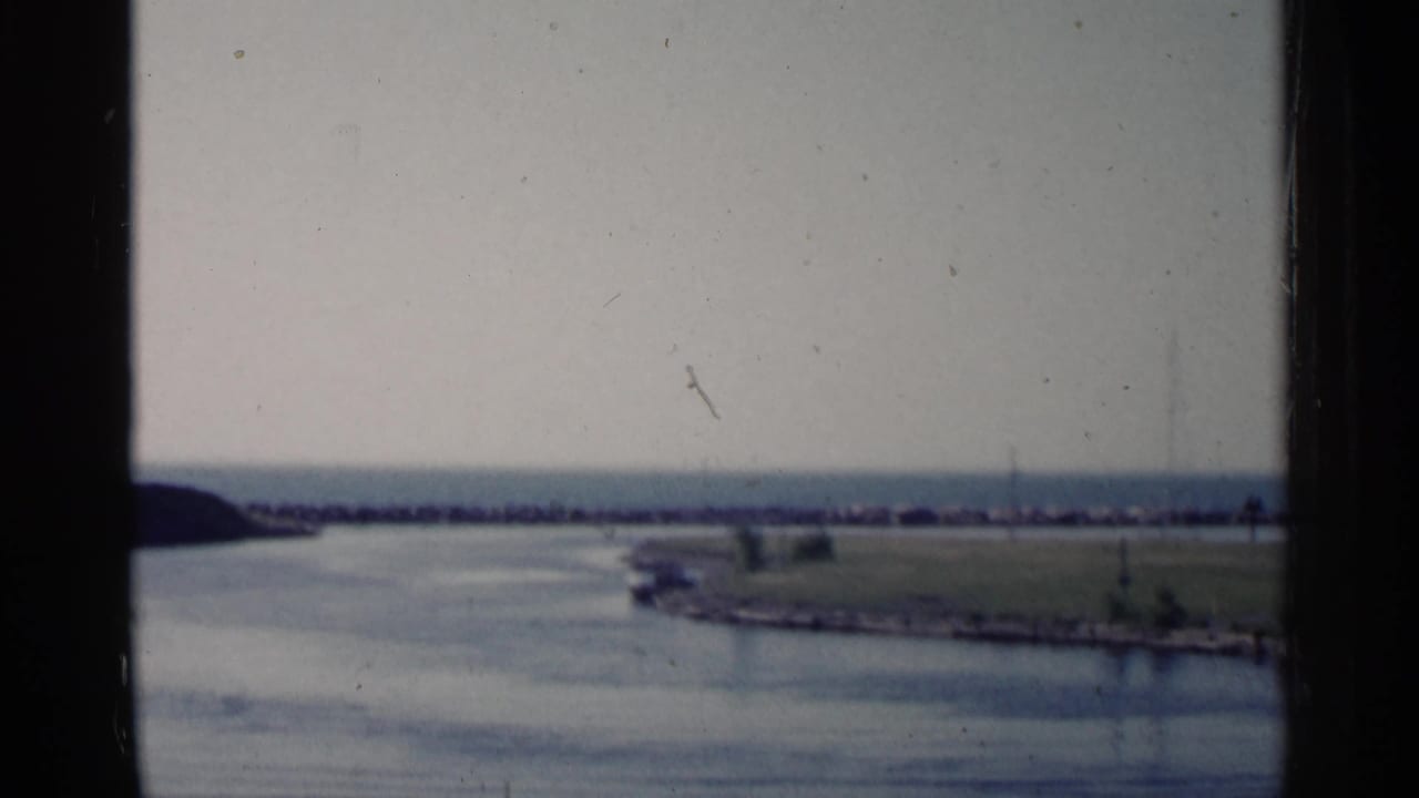 Distant breakwater and low shoreline beyond calm water, partly framed by a window.