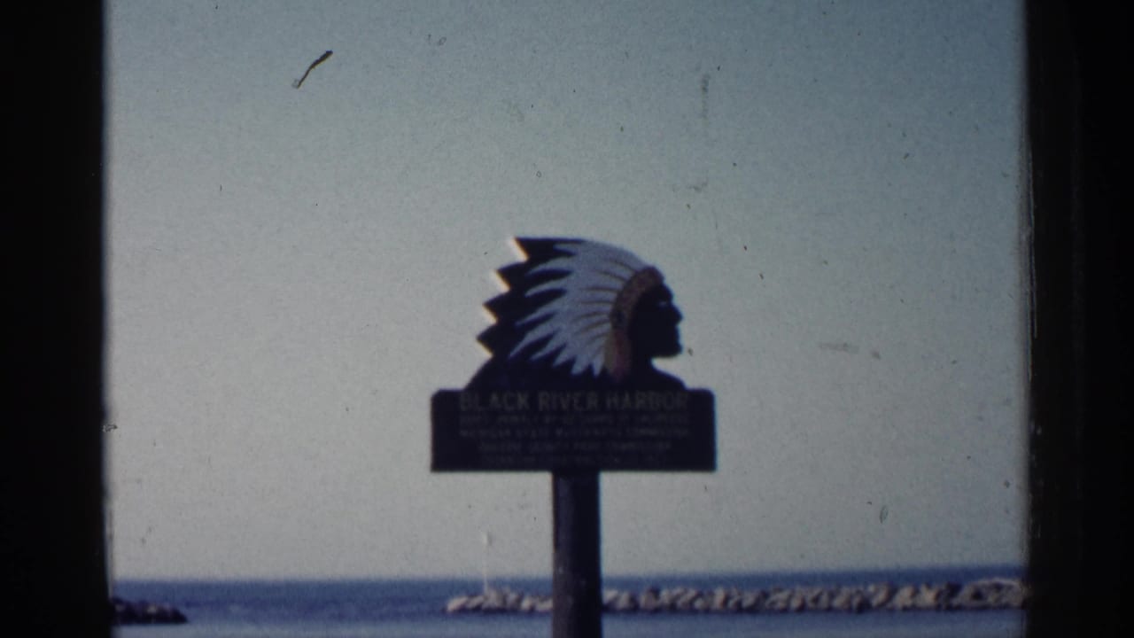 Black River Harbor sign centered against pale sky, water, and breakwater.
