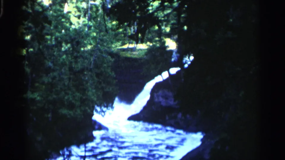 1960 Michigan 8mm frame of a bright waterfall flowing through a wooded stream channel.