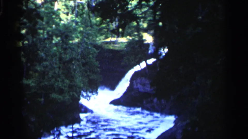 1960 Michigan 8mm frame showing a forest waterfall cascading into rippled water below.